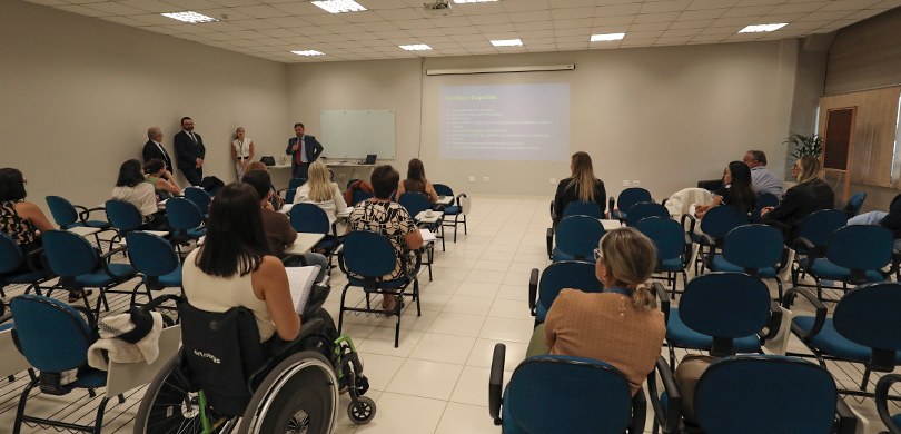 Fotografia de um ambiente interno de treinamento ou palestra, com diversas pessoas sentadas e em...