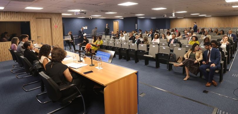 Servidores participam de seminário sobre equidade racial em Brasília Fotografia de um auditório com homens e mulheres sentados em cadeiras com estofado cinza-claro. ...