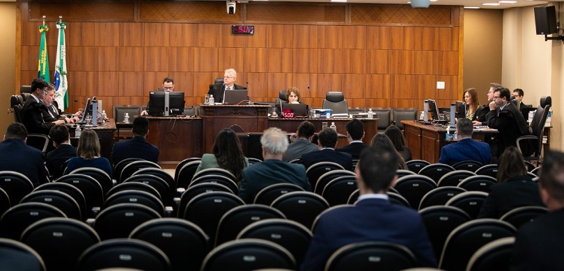 Foto em que aparecem os membros da Corte do TRE-PR, sentados atrás de mesas de madeira escura. M...