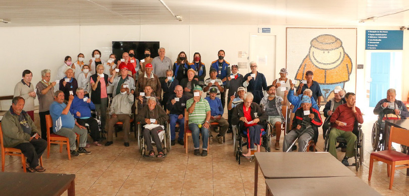 Socorro aos Necessitados - Lar dos Idosos terá seção eleitoral em Curitiba Fotografia de várias pessoas em uma sala, todas elas estão segurando um papel e posando para a f...