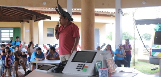 Fotografia em ambiente externo na qual se vê um grupo de homens em pé interagindo. À direita, em...
