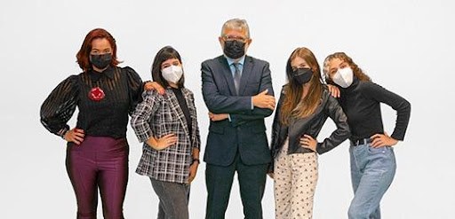 Fotografia de cinco pessoas posando com um fundo branco. São quatro mulheres e um homem que está...