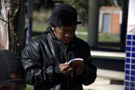 Uma pessoa com cabelos escuros e uma jaqueta preta de couro, com um boné virado para trás, segur...