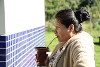 Uma mulher de perfil, com uma jaqueta de lã cor de creme, bebe de uma cuia de chimarrão com uma ...