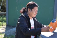 Um homem com jaqueta preta sobre uma camiseta branca e cabelos escuros presos para trás olha par...