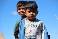 Dois meninos estão em pé em um campo sob um céu azul claro. O menino em primeiro plano, com uma ...