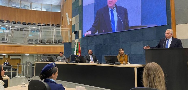 Fotografia em que aparecem dois homens e uma mulher sentados à mesa do plenário da Câmara de Lon...