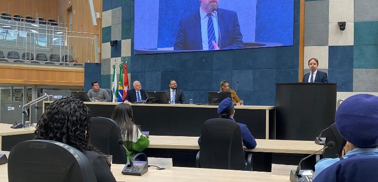 Fotografia em que aparecem dois homens e uma mulher sentados à mesa do plenário da Câmara de Lon...