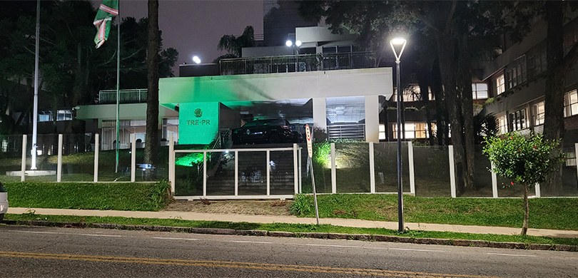 Fotografia tirada à noite da fachada do edifício-sede do TRE-PR. Há uma iluminação verde na fren...