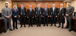 Fotografia da Corte do TRE-PR na sala de sessões. É possível ver nove homens de terno, dos quais...