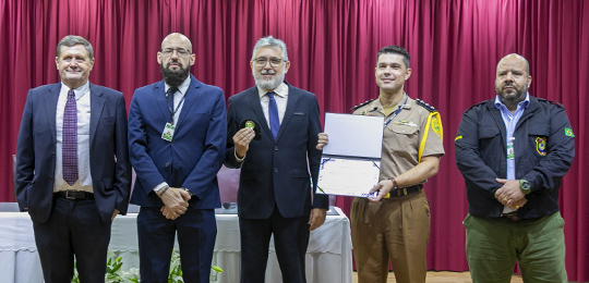 TRE-PR apresenta processo eleitoral para cadetes da Polícia Militar 3 Fotografia de cinco homens posando para a foto em um palco. Três deles usam terno, os outros doi...