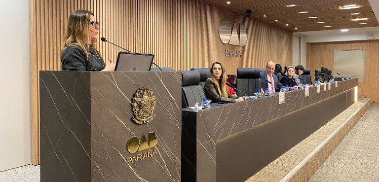 Fotografia que pega a mesa de honra do auditório da OAB-PR em diagonal, da esquerda para a direi...