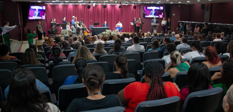 Foto de um auditório, em que se observam, em primeiro plano, pessoas sentadas de costas, a maior...