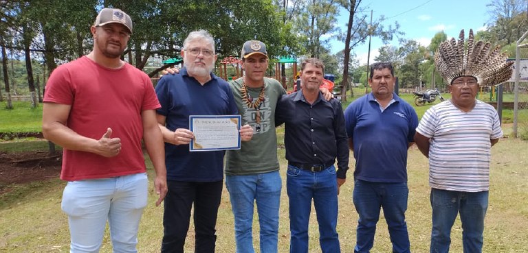 Fotografia de seis homens posando sorrindo alinhados. Um dos homens segura um certificado em mão...