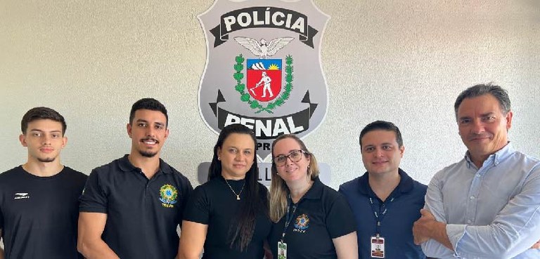 Fotografia de duas mulheres e quatro homens posando sorrindo. Uma mulher e um homem vestem uma c...