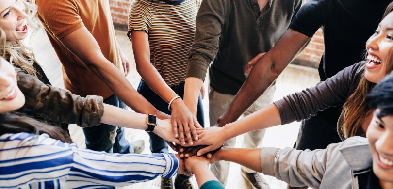 Foto de oito mãos sobrepostas, em que quatro são mulheres e quatro são homens.