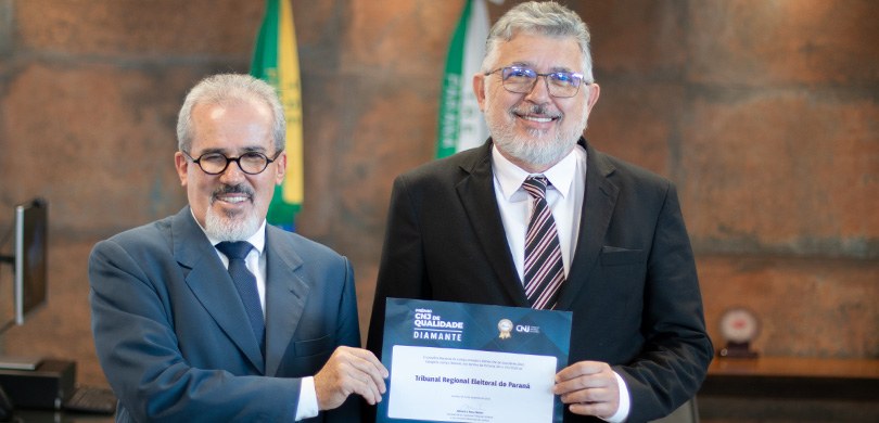 Fotografia de dois homens posando para foto sorrindo enquanto seguram um certificado. Os dois us...