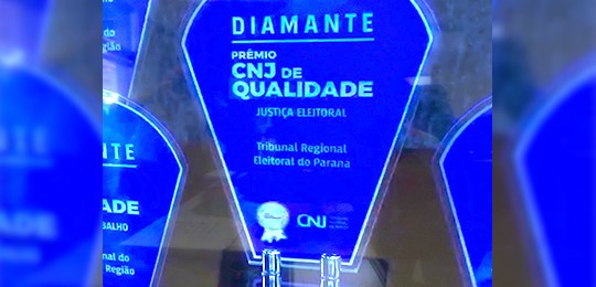 Fotografia de um trofeu azul onde está escrito Diamante Prêmio CNJ de Qualidade Justiça Eleitora...