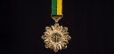 Imagem de uma medalha pendurada em um cordão verde e amarelo sobre um fundo inteiramente preto. ...