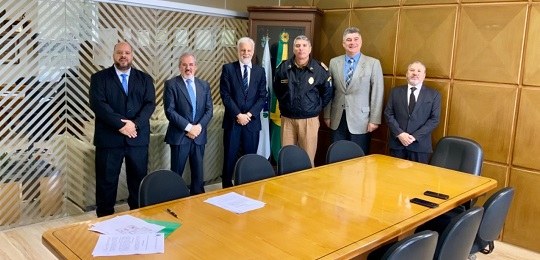TRE-PR firma acordo com Secretaria de Segurança Fotografia de um grupo de pessoas em pé em uma sala. Há uma mesa de trabalho e cadeiras ao seu r...