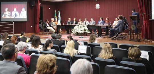 TRE-PR lança projeto Mulheres na Política. Inscrições estão abertas! Fotografia de um auditório. Na plateia, há pessoas sentadas de costas para a câmera. Ao fundo, s...