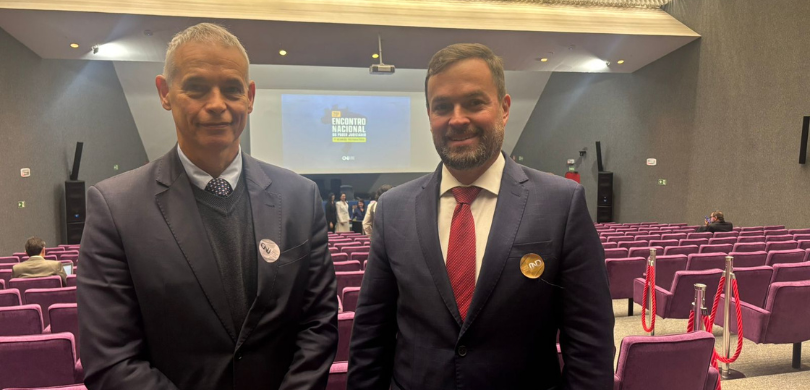 TRE-PR participa da 1ª reunião preparatória para o 20º ENPJ Fotografia em que se observam dois homens, de pele clara, posando para foto em um auditório. Em ...