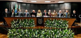 Fotografia da mesa de autoridades composta por 12 pessoas, entre homens e mulheres, em um palco ...