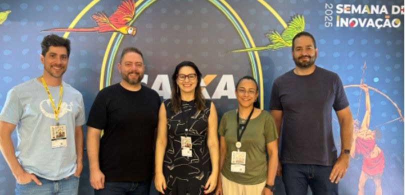 Fotografia na qual é possível ver duas mulheres e três homens sorrindo e posando para a foto. Ao...