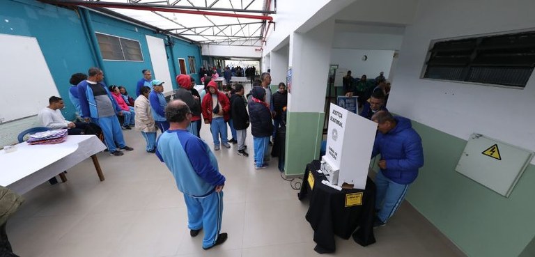 Fotografia em que se veem várias pessoas usando uniformes azuis esperando em filas para votar em...