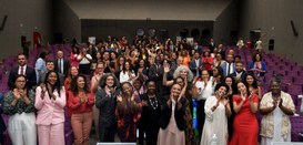 Na imagem, tirada do palco de um auditório, vêem-se na plateia várias pessoas, em sua maioria ne...