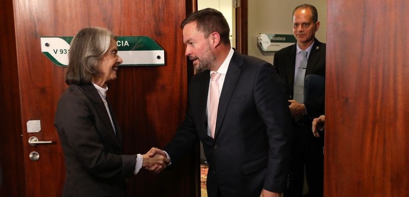 Fotografia na qual se observa o aperto de mãos entre uma mulher e um homem (a ministra Cármen Lú...