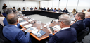 Fotografia de uma sala de reuniões institucional onde diversas pessoas, homens e mulheres de ida...