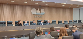Fotografia que retrata um plenário institucional durante um evento. Ao fundo, centralizado em um...