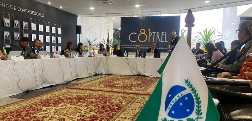 TRE-PR participa do 81° Encontro do Colégio de Presidentes dos Tribunais Regionais Eleitorais (Coptrel) Fotografia de uma mesa de autoridades, em formato retangular. Ao centro, há um tapete estampado....
