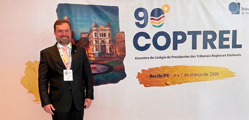 Fotografia de um homem de pele clara, barba e cabelos castanhos, vestindo terno preto, camisa br...