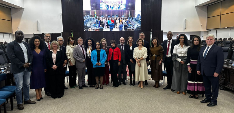 Fotografia de diversas pessoas, entre homens e mulheres, posando sorrindo, organizadas em meio c...