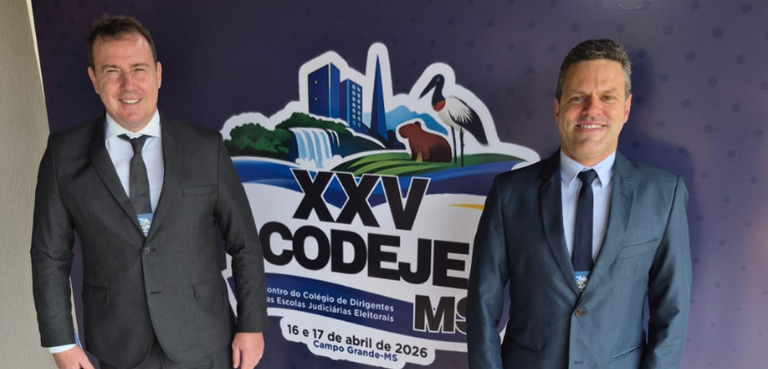 Fotografia de dois homens, de pele clara e cabelos curtos e escuros, posando lado a lado e sorri...