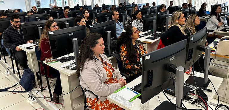 Fotografia de várias pessoas, entre homens e mulheres, sentados em carteiras com computadores e ...