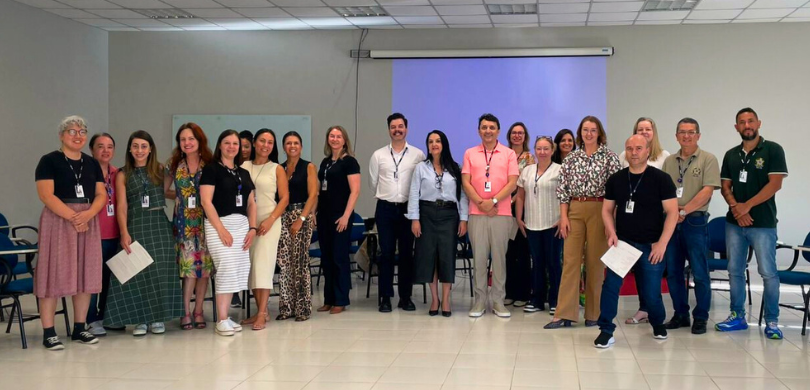 Na fotografia, veem-se homens e mulheres posando sorrindo, uns ao lado das outras. Eles vestem d...