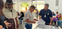 Fotografia de dois homens diante de uma urna eletrônica. Um deles é servidor da Justiça Eleitora...