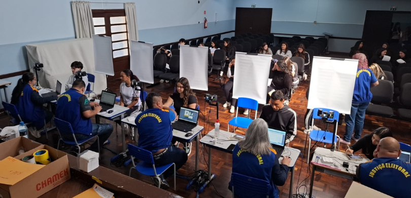 Fotografia, vista de cima, de estudantes recebendo atendimento por representantes da JE, em guic...