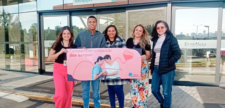 TRE-PR realiza mutirão de doação de sangue em parceria com o Hospital Erasto Gaertner 2 Cinco pessoas estão sorrindo para a foto. Elas estão segurando um cartaz que diz: Compartilhe co...