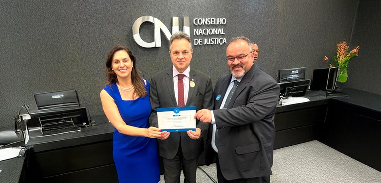 TRE-PR recebe o Selo Linguagem Simples Na fotografia veem-se três pessoas, dois homens e uma mulher. Ela tem cabelos lisos na cor casta...