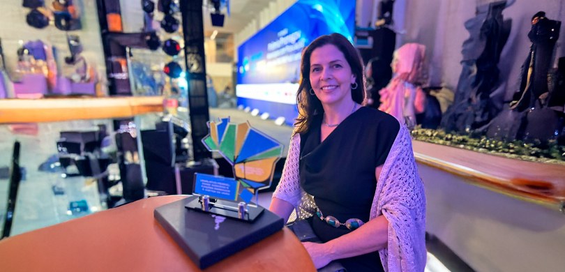 Fotografia da servidora Rachel Diogenes Ramina Rezler posando sorrindo sentada ao lado de uma me...