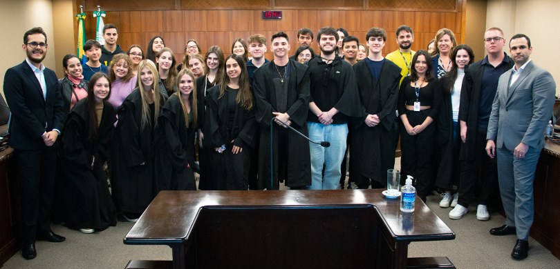 TRE-PR recebe universitários da FAE no Projeto Tribunal Eleitoral Jovem A fotografia mostra um grupo com cerca de 30 pessoas posando e sorrindo para a câmera. Eles estã...