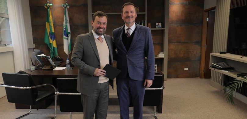 Fotografia na qual se observam dois homens, de pele clara e cabelos escuros, sorrindo e posando ...