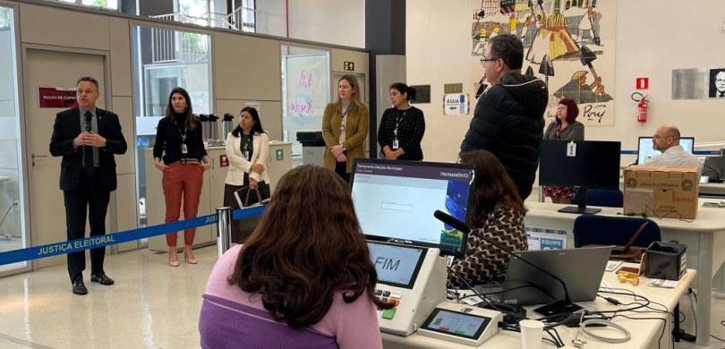 Foto em que aparecem várias pessoas em pé, voltadas para o desembargador Panza, que fala. Em pri...