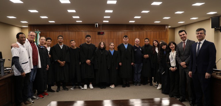 Posam para a foto estudantes vestidos de toga. À sua direita, estão dois homens vestidos com um ...