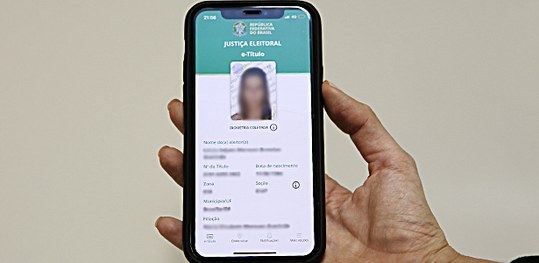 Foto de uma mão segurando um celular com o aplicativo e-Título aberto