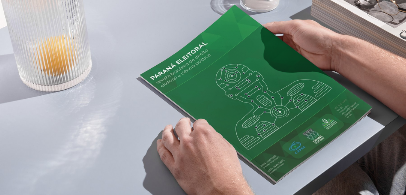 Última edição da Revista Paraná Eleitoral 2025 já está disponível Na imagem, veem-se dois braços apoiados em cima de uma mesa cinza, segurando a revista “Paraná E...